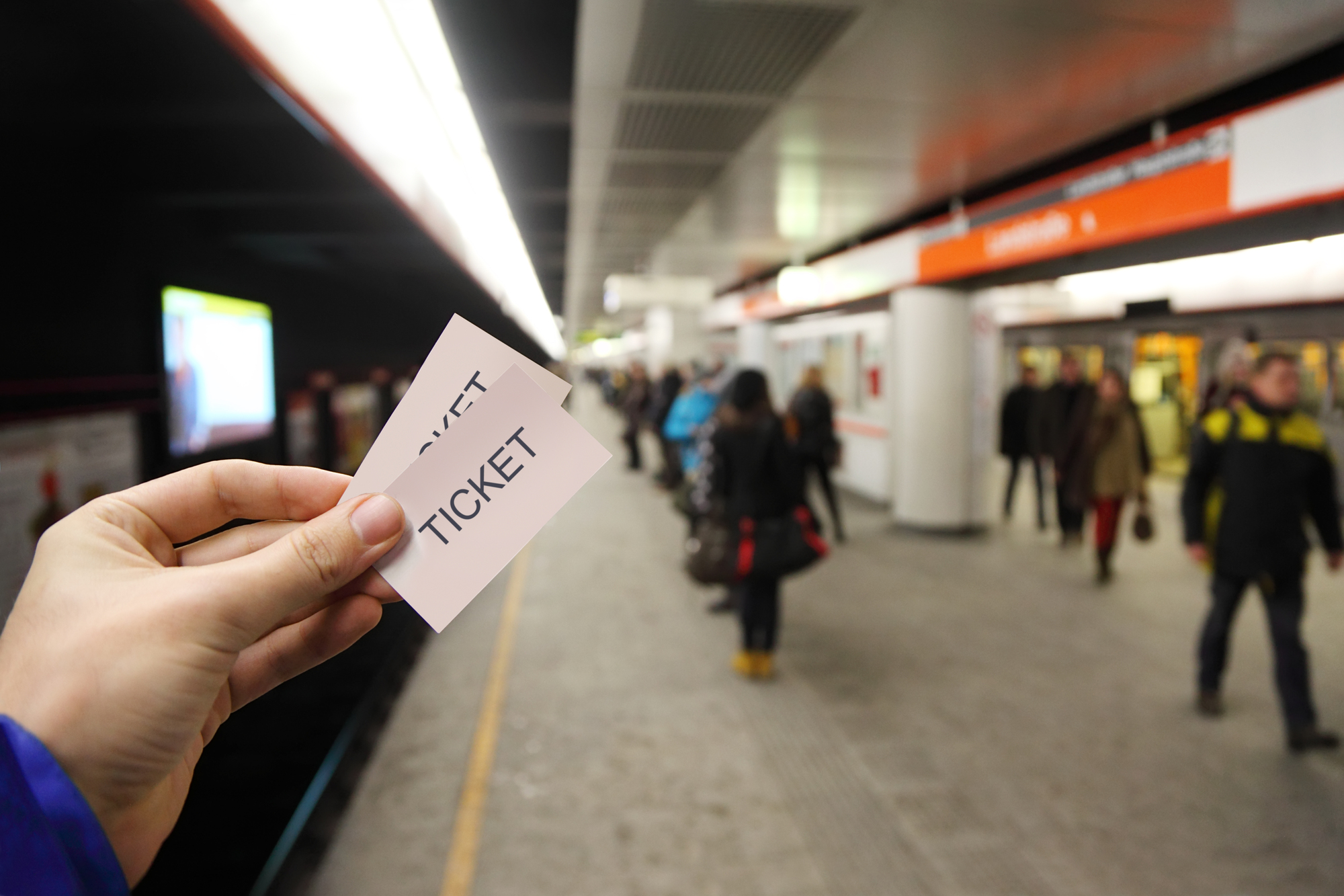 Male hand holds two tickets in subway. People wait for train on platform.
